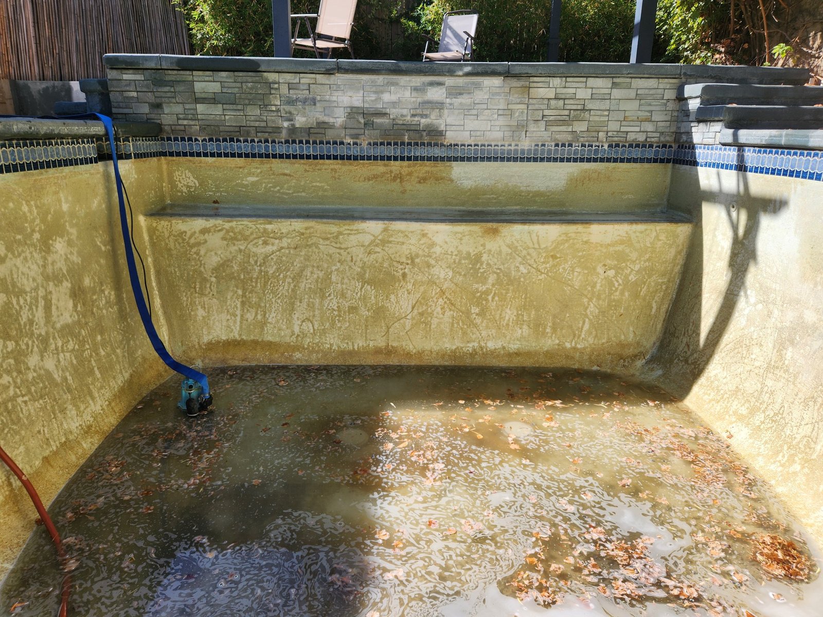 Stained deep end and bench with murky water before an acid wash in Roseville, CA